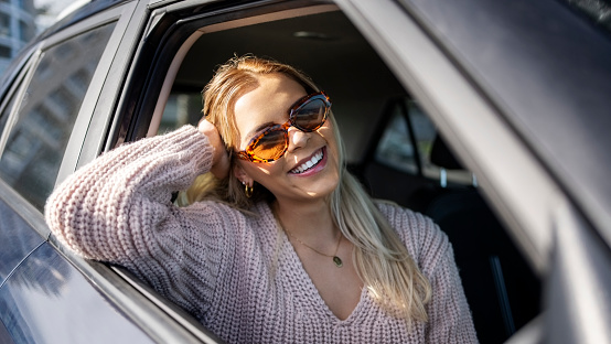 Beautiful young woman with sunglasses traveling by a car looking outside window and smiling during summer day