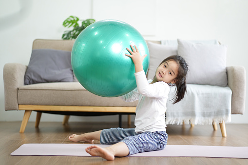 Little Asian girl playing fitness bouncing ball for exercise in the living room