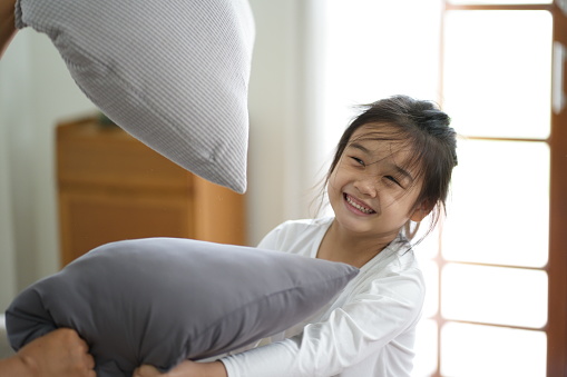 Colse up of little Asian girl having a pillow fight in the livingroom