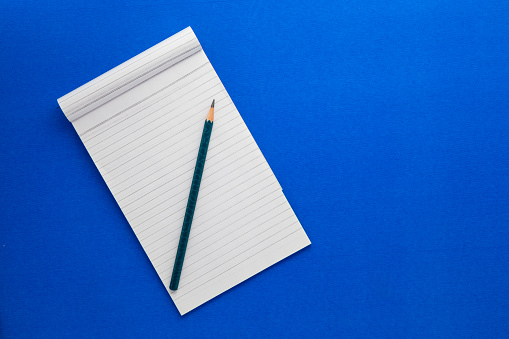 Top view of a open notebook with pencil on a blue background, school notebooks with a spiral spring, office notepad flat lay.
