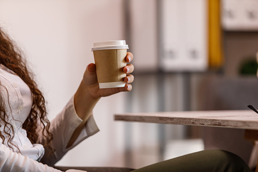 A snapshot of a businesswoman holding a disposable coffee cup, taking a moment to relax and recharge.