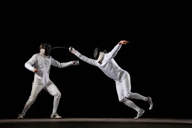 Two fencer in a fencing pose. One is attacking and one is defending. White on black background. Point.