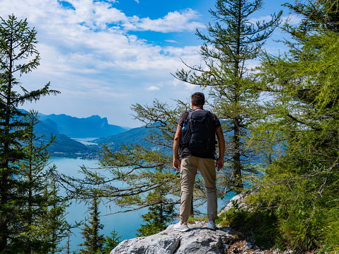 a traveler with a backpack stands on a mountain against the backdrop of Lake Attersee, Austria