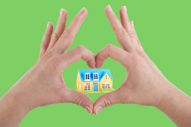 istock Hands making a heart shape with house on green background 1635502880