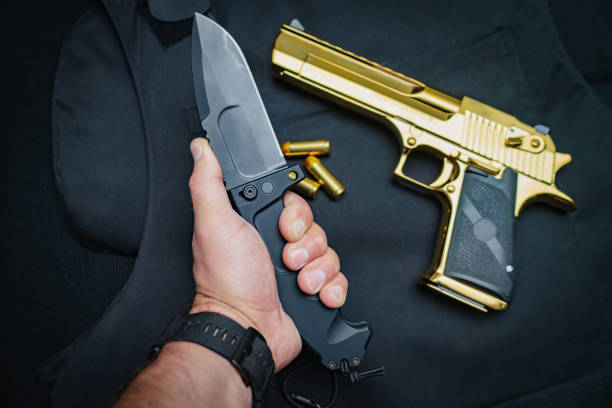 istock Melee weapons and firearms. Folding tactical knife and pistol Desert eagle gold. 1635503431