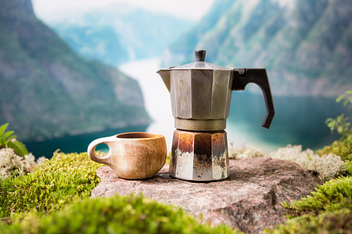 Morning coffee with a Moka coffee maker and a traditional wooden Finnish cup Kuksa in a tourist camp against the backdrop of a Scandinavian landscape