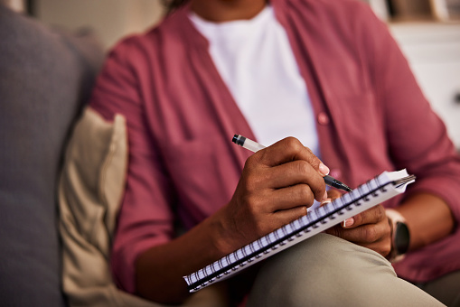 A woman holding a notebook and writing notes with a pen, sitting on a couch.