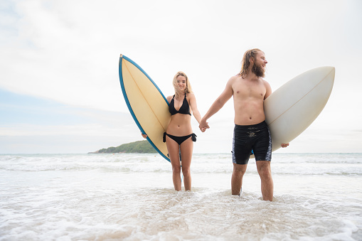 Couple of surfers holding hands and looking at each other on beach