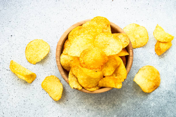 istock Potato chips in wooden bowl on white table. Top view. 1635559666