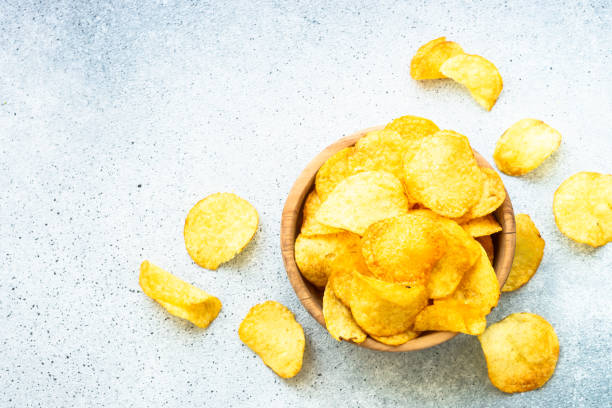 istock Potato chips in wooden bowl on white table. Top view. 1635560180
