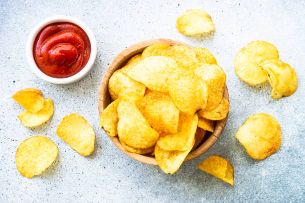 istock Potato chips in wooden bowl on white table. Top view. 1635560185