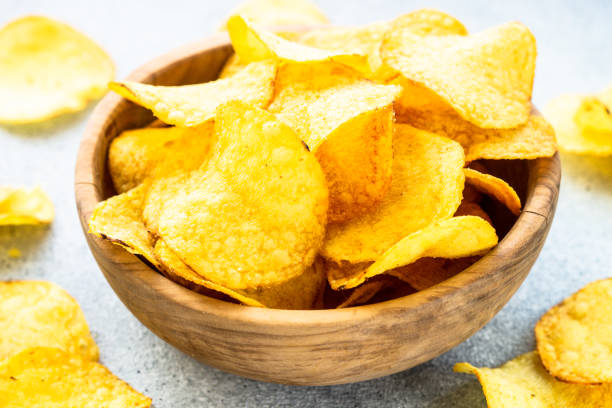 istock Potato chips in wooden bowl on white table. Top view. 1635560201