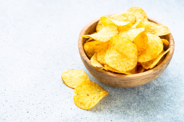 istock Potato chips in wooden bowl on white table. Top view. 1635560262