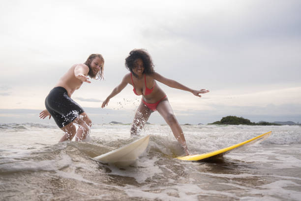 istock Couple surfing on the beach having fun and balancing on the surfboard 1635562108