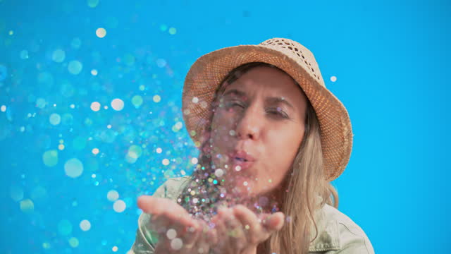 SLO MO LD Young woman blowing glitter off her hands towards the camera