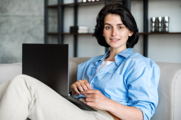 istock Woman freelancer sitting on couch with laptop and looking at camera 1635576736