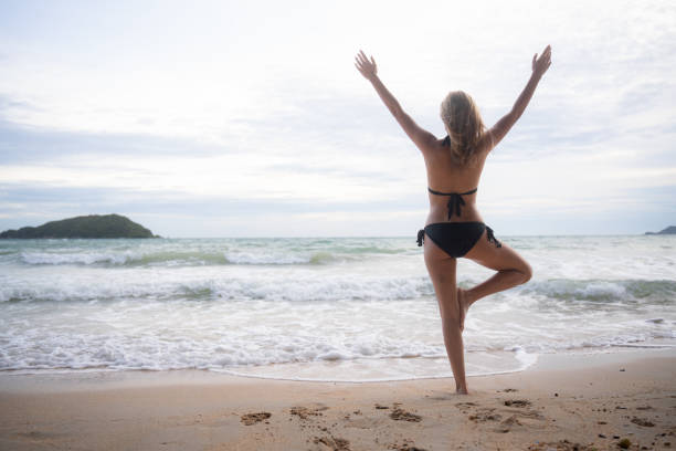 istock Young woman in black bikini practicing yoga on the beach at sunset. 1635577255