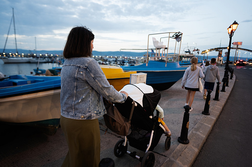 Mother with baby carriage on the pier in the evening, back view.