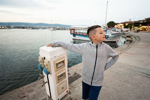 Young boy standing on the pier near the sea.