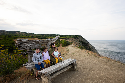 Happy family sitting on bench at seaside in the countryside during summer. Cape Emine, Black sea coast, Bulgaria.