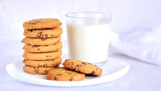 cookies with chocolate chips on a white plate on a light background next to a glass of milk. selective focus