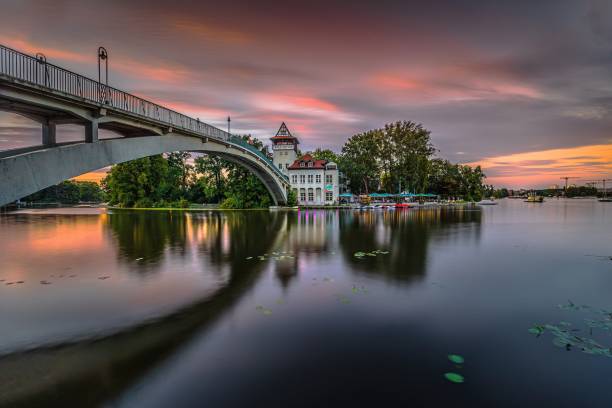Sunset in Berlin with colorful sky. Bridge over the Spree to the Insel der Jugend in the evening in summer. Illuminated culture house with beer garden. Reflection on the water surface.