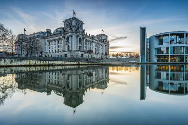 Government district in Berlin on a winter day. Reichstag and Paul Löbe House in the evening at sunset. River Spree with reflection on water surface of government buildings. Clouds in the sky
