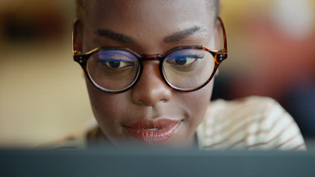 Business woman, happy and reading on computer for online article, editing newsletter or website planning. African person, editor or writer with smile for blog and screen reflection in her glasses
