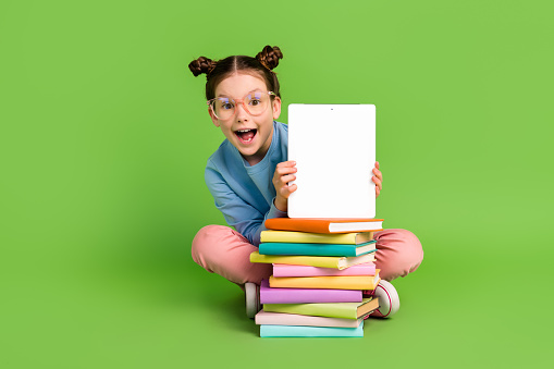 Full size photo of impressed schoolgirl dressed blue sweatshirt sit with book presenting display isolated on green color background.
