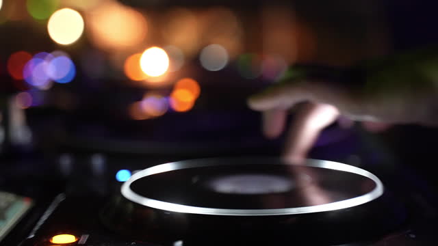 DJ hands mixing music turntable console control panel at illuminated nightclub party closeup