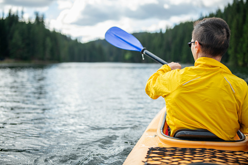 Man paddles kayak across calm water in mountain lake.