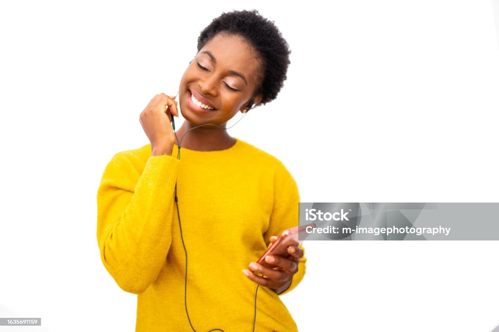 young African American woman holding mobile phone and enjoying music with earphones against isolated white background Portrait young African American woman holding mobile phone and enjoying music with earphones against isolated white background Music Stock Photo