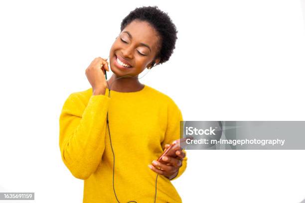 Young African American Woman Holding Mobile Phone And Enjoying Music With Earphones Against Isolated White Background Stock Photo - Download Image Now