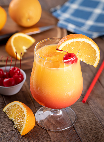 Tequila sunrise cocktail with cherry and orange slice on rustic wooden table