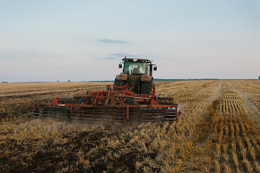 Modern tractor with a heavy trailed disc harrow works a wide hilly field. Autumn or spring agricultural campaign