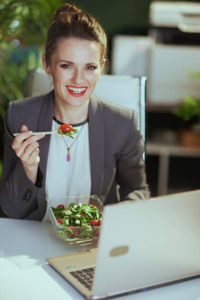 istock smiling female employee in green office eating salad 1635772479
