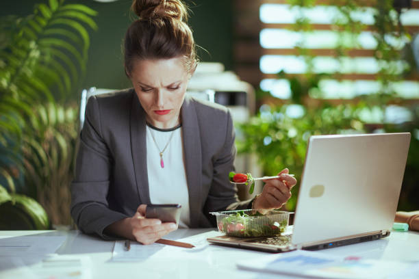 istock woman worker in green office eating salad and using phone 1635772492