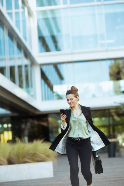 istock female employee in business district using phone and walking 1635778042