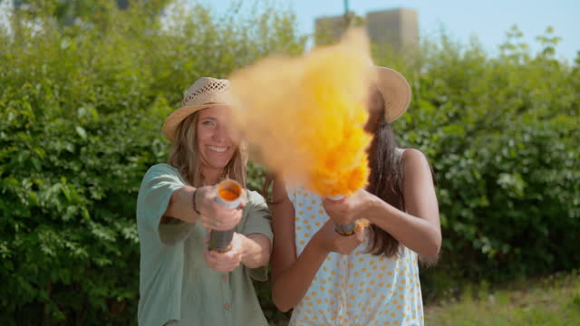 SLO MO Two women shooting orange dust from a handheld powder cannon
