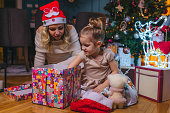 Beautiful happy young mother with her little daughter unboxing Christmas presents