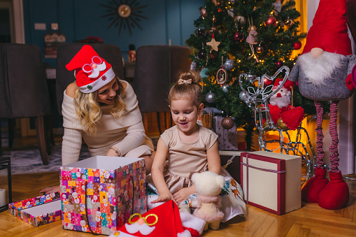 Beautiful happy young mother with her little daughter unboxing Christmas presents on the floor