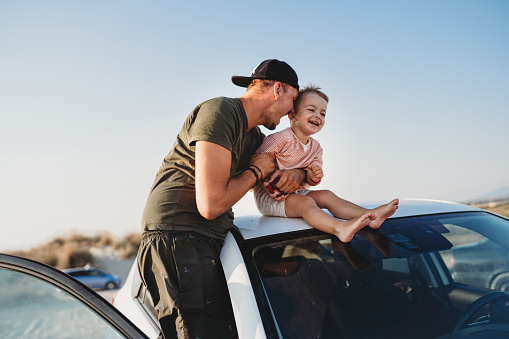 Young father and his son sitting on the roof of his car