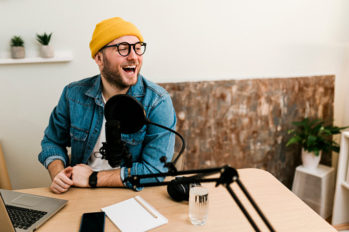 Young smiling man recording podcast and doing live streaming using microphone and headphones in recording studio