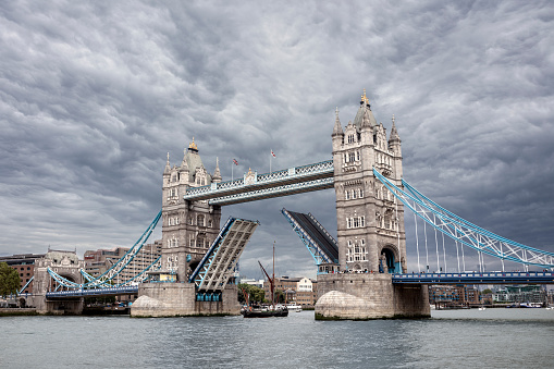 Tower Bridge in London, England raised up open for boat to pass under with stormy cloud above