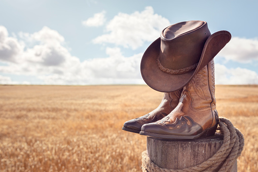Sombrero de vaquero, botas y fondo de campo de trigo en establos de rancho, concierto en vivo del festival de música country o concepto de baile en línea photo