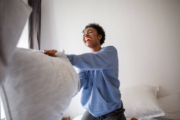 happy young African American woman having pillow fight in bedroom stock photo