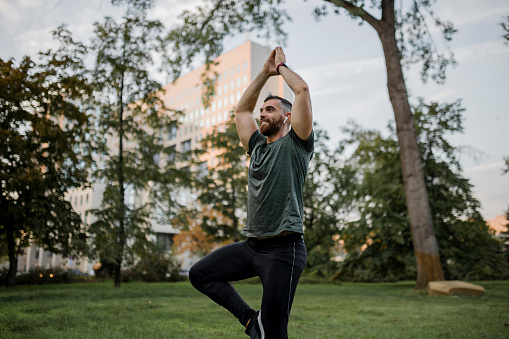 Smiling attractive man practicing yoga concept, standing in Vrksasana exercise, Tree pose, working out, wearing sportswear,