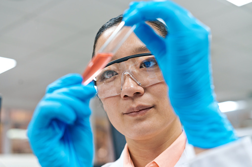 Female researcher wearing protective eyeglasses while examining chemical in test tube at laboratory