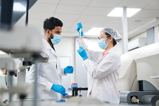 Male and female medical workers examining chemicals while standing in laboratory