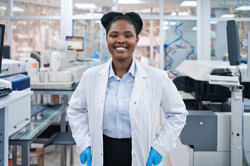 Portrait of smiling young female scientist with hands in pockets standing at laboratory